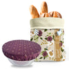 Floral-patterned bread bag with bread and a purple dish cover on a white background