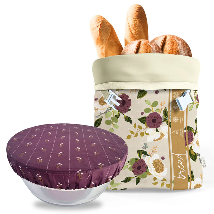 Floral-patterned bread bag with bread and a purple dish cover on a white background