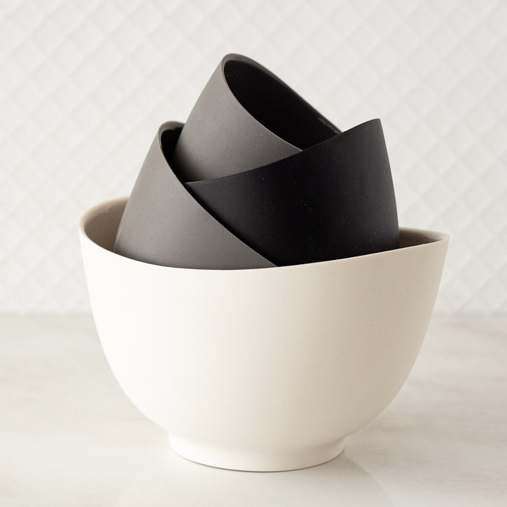 A set of four silicone bowls in varying sizes, with a white bowl on the bottom,  two grey bowls and a black bowl stacked inside of it.
