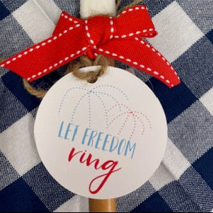 Decorative tag with firework design, red ribbon, and 'Let Freedom Ring' tag on a blue and white checkered background.