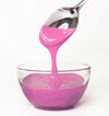 Pink frosting being spooned into a glass bowl on a white background
