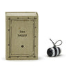 A porcelain bee figurine inside a cardboard matchbox with the text 'Bee happy' on the front.