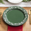 Green plate with decorative white patterns on a wooden table with gold cutlery and a red napkin.