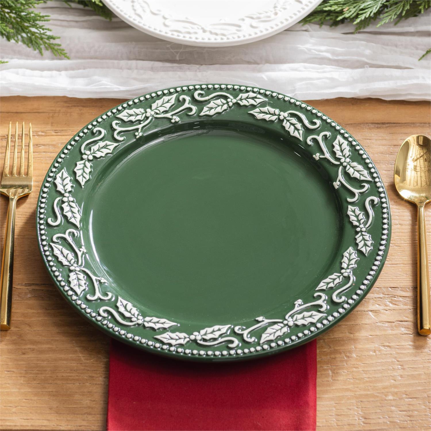Green plate with decorative white patterns on a wooden table with gold cutlery and a red napkin.