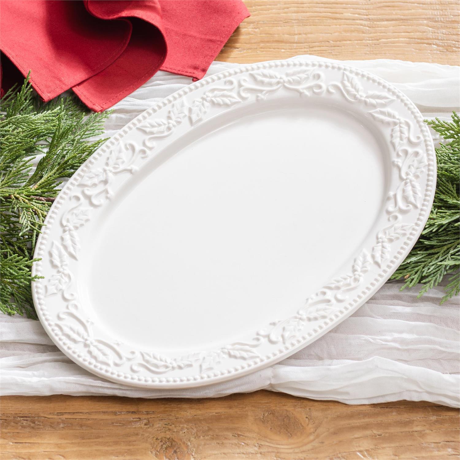 White decorative oval platter on a wooden surface with greenery and a red cloth.