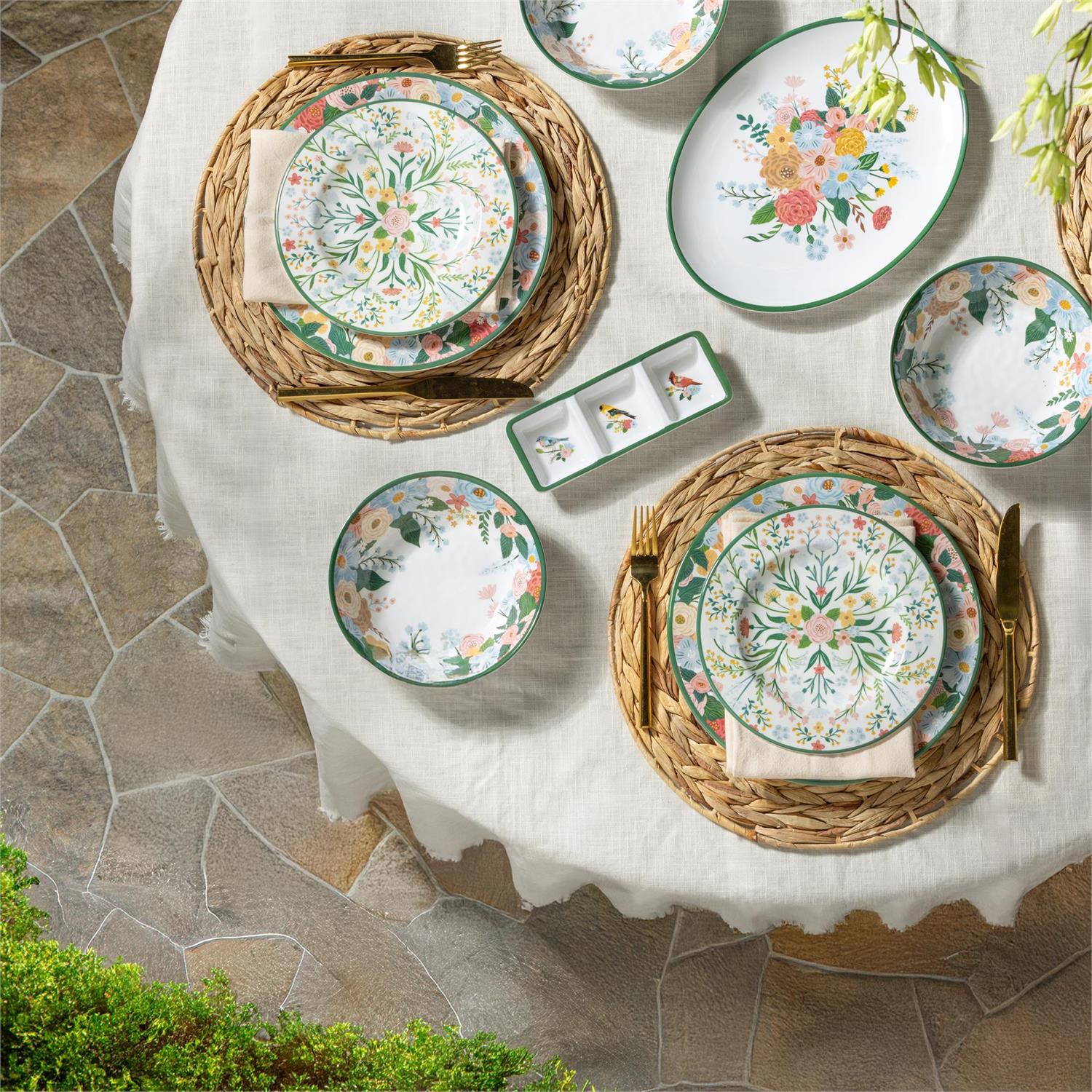 Decorative table setting with floral plates and wicker chargers on a stone patio.