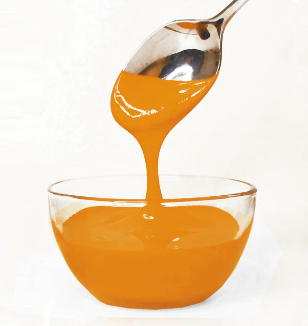 Orange frosting being poured from a spoon into a glass bowl on a white background
