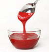 Red frosting being poured from a spoon into a clear glass bowl on a white background