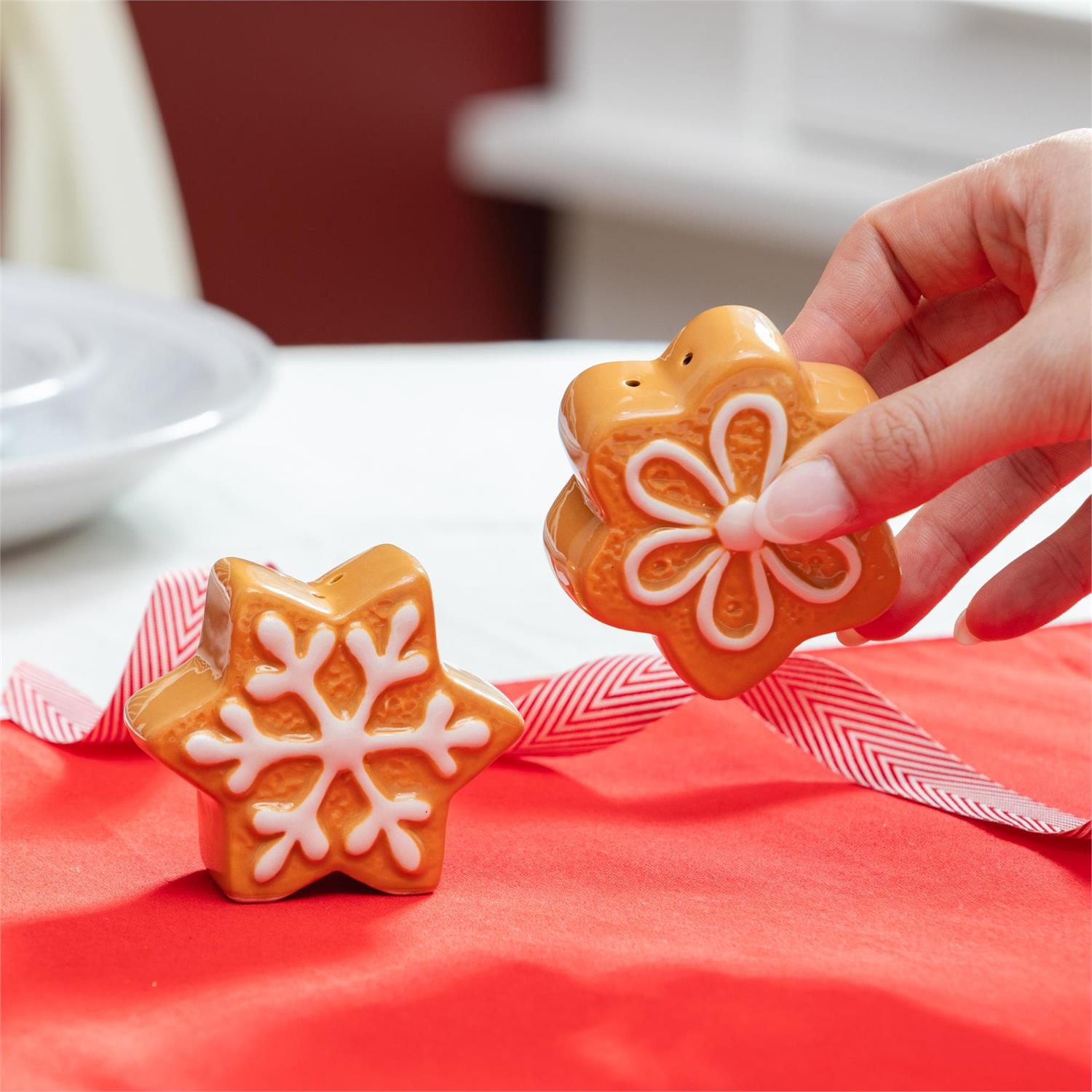 Decorative gingerbread cookie salt and pepper shakers with white icing decoration on a red surface