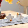 Two ghost-shaped salt and pepper shakers with pumpkins on a tablecloth.