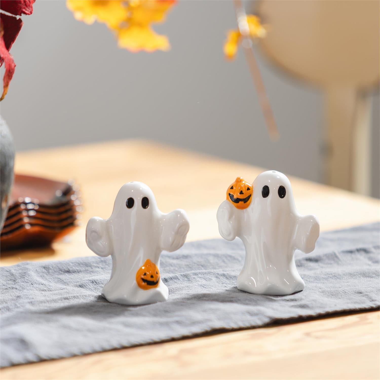 Two ghost-shaped salt and pepper shakers with pumpkins on a tablecloth.