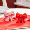 Pink and red bow-shaped salt and pepper shakers on a red surface with blurred background