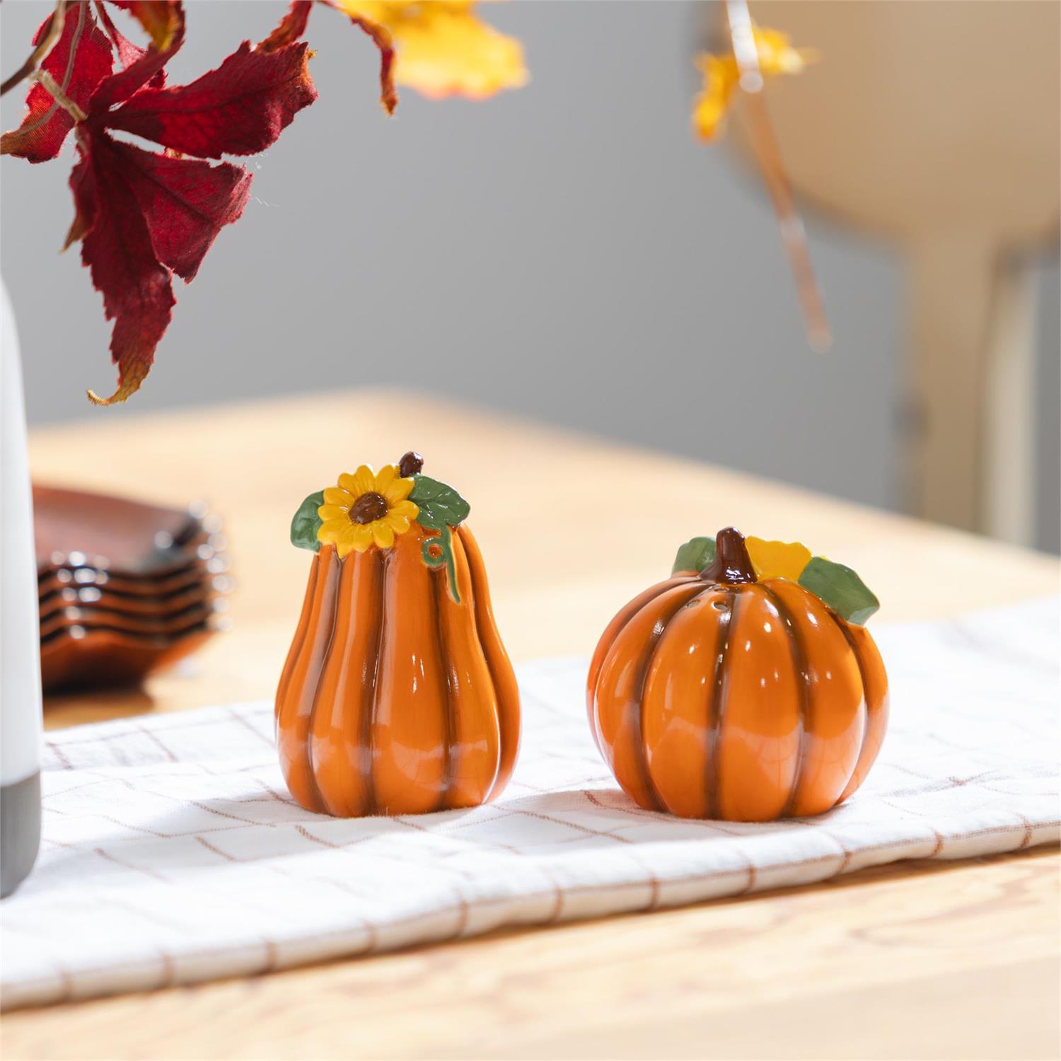 Two decorative pumpkins salt and pepper shakers with sunflower designs on a table with autumn leaves.