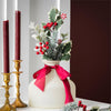 Decorative Christmas greenery stem including berries, holly, and a red ribbon, set against a neutral background.