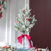Decorative arrangement with greenery, red berries, and a red ribbon in a clear glass vase against a neutral background.