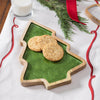 Three cookies on a Christmas tree-shaped plate with a glass of milk and festive decorations.