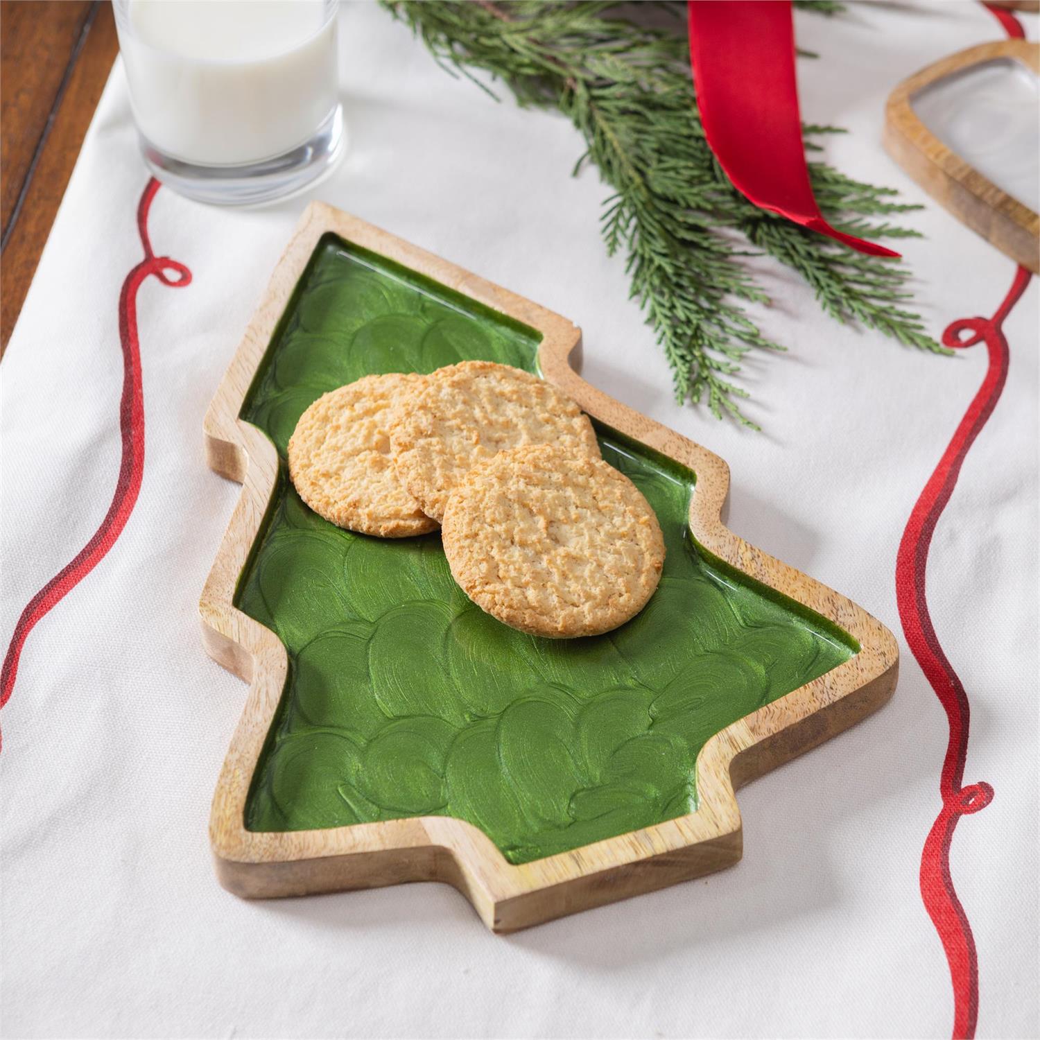 Three cookies on a Christmas tree-shaped plate with a glass of milk and festive decorations.
