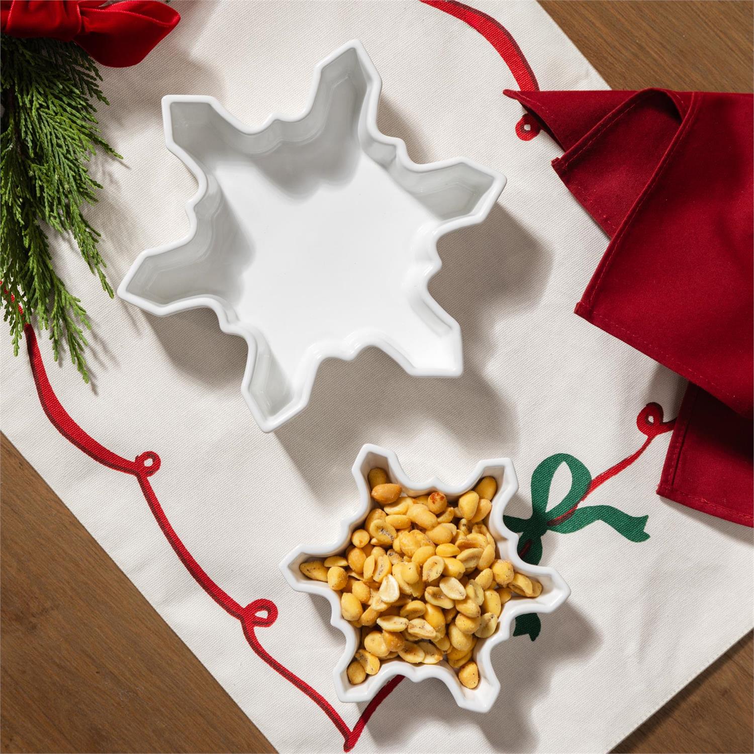 White snowflake-shaped serving dishes on a decorative tablecloth with pine branches and red napkins.