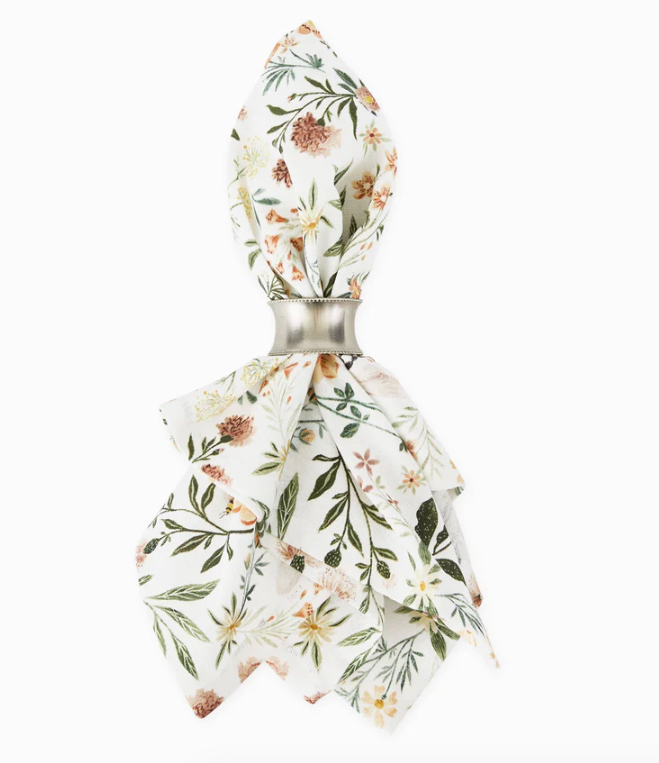 A cloth napkin with floral and greenery design in a silver napkin ring on a white background