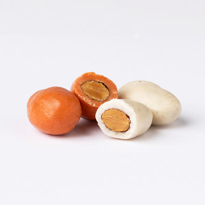 Four round candies, two orange and two white, with an almond in the middle on a white background.