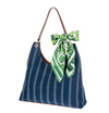 Blue striped handbag with a green and white scarf tied around the handle on a white background
