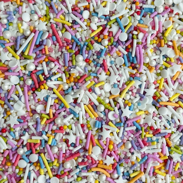 A close-up of colorful sprinkles and candy pieces, including white pearls, white stars, pink, yellow, blue and green jimmies, filling the entire frame.