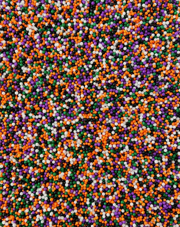 A close-up of small round sprinkles in four classic colors: orange, purple, white, and green.