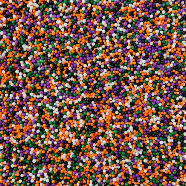 A close-up of small round sprinkles in four classic colors: orange, purple, white, and green.