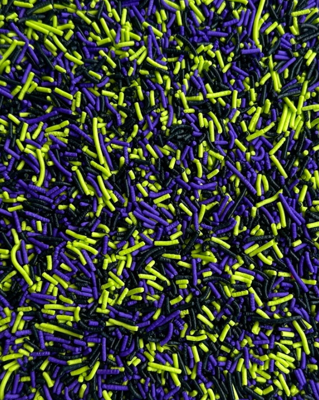 A close-up, view of sprinkles in three colors: bright purple, neon lime green, and black.
