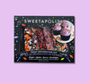 Sweetapolita Halloween treat decorating kit in a black box with colorful sprinkles, and decorated cupcakes visible through a clear window, set against a solid lavender background.
