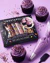 Sweetapolita Halloween treat decorating kit with a black box containing decorated treats, shown with purple-frosted cupcakes, a piping bag, sprinkles, and a spatula on a lavender background.