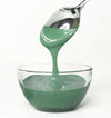 Green frosting being spooned into a glass bowl on a white background