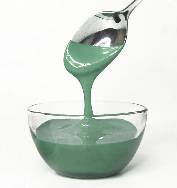 Green frosting being spooned into a glass bowl on a white background