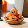 Stack of Halloween-themed orange fabric pumpkins in a wooden bowl on a table.