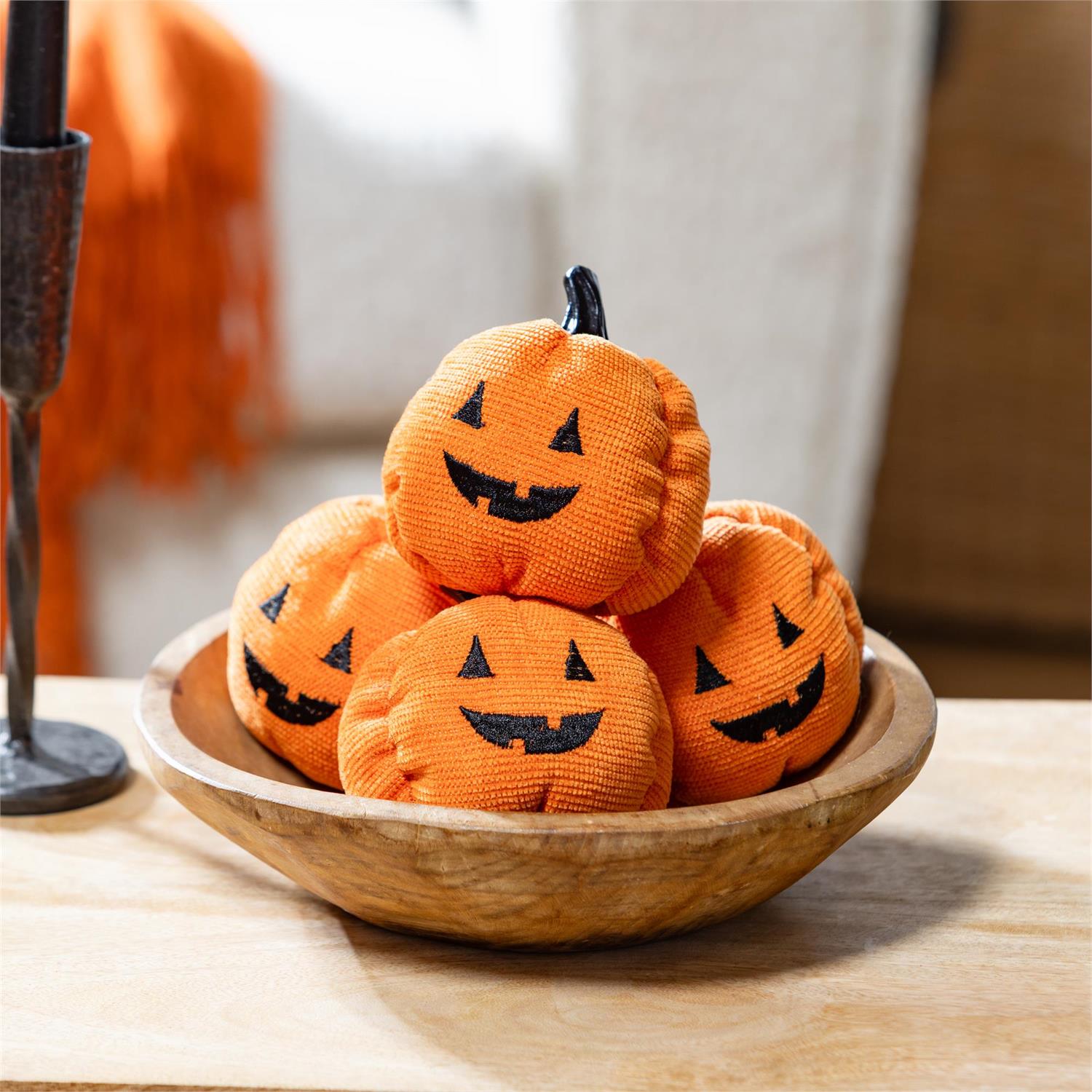 Stack of Halloween-themed orange fabric pumpkins in a wooden bowl on a table.