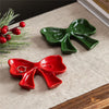 Two ceramic bow-shaped trinkets, one red and one green, on a textured surface with a branch of holly.