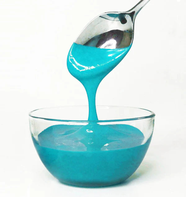 Blue frosting being spooned into a glass bowl on a white background