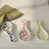 Three ceramic spoon rests with blueberry, cherry, and lemon patterns on a light surface.