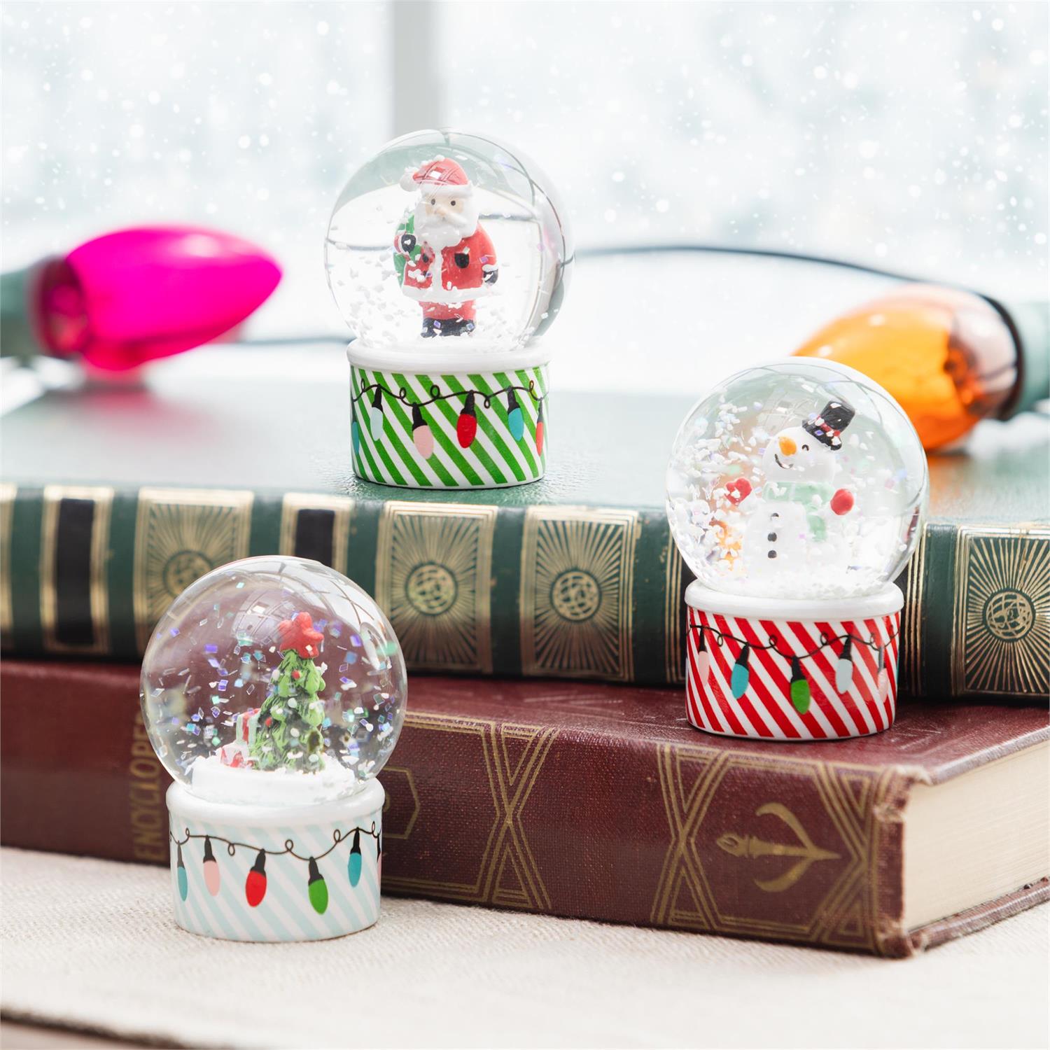 Three Christmas-themed snow globes on top of books with decorative bases.
