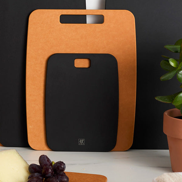 Set of cutting boards in black and brown on a kitchen counter with a plant.