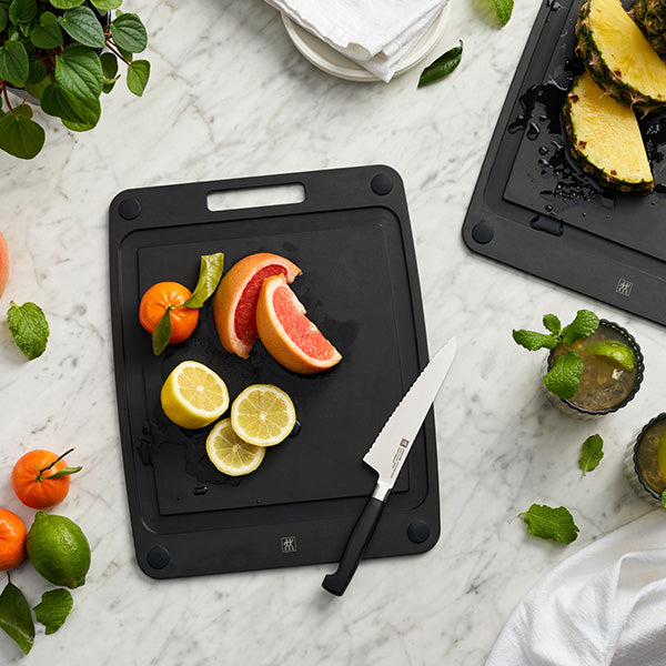 Black cutting board with sliced citrus fruits and a knife on a marble surface.