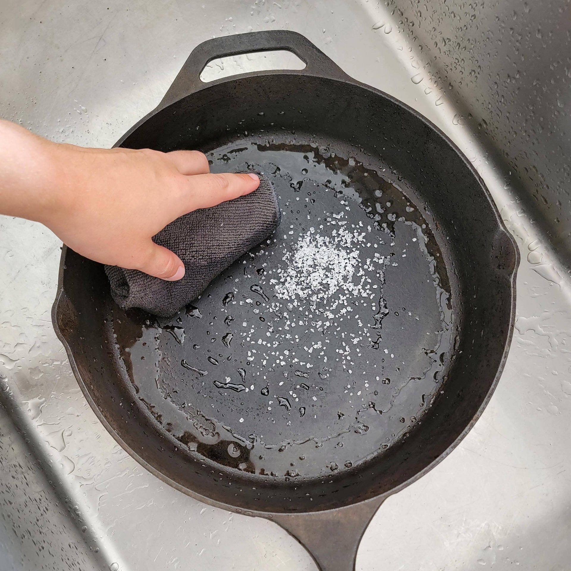 Person cleaning a cast iron skillet with a sponge in a sink.