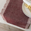 Woven table runner on a wooden table with a white plate and gold fork.