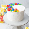 Colorful frosted cake on a white stand with frosting packets in the background.