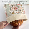 Floral-patterned beeswax wrap being used to cover a loaf of bread on a white surface.