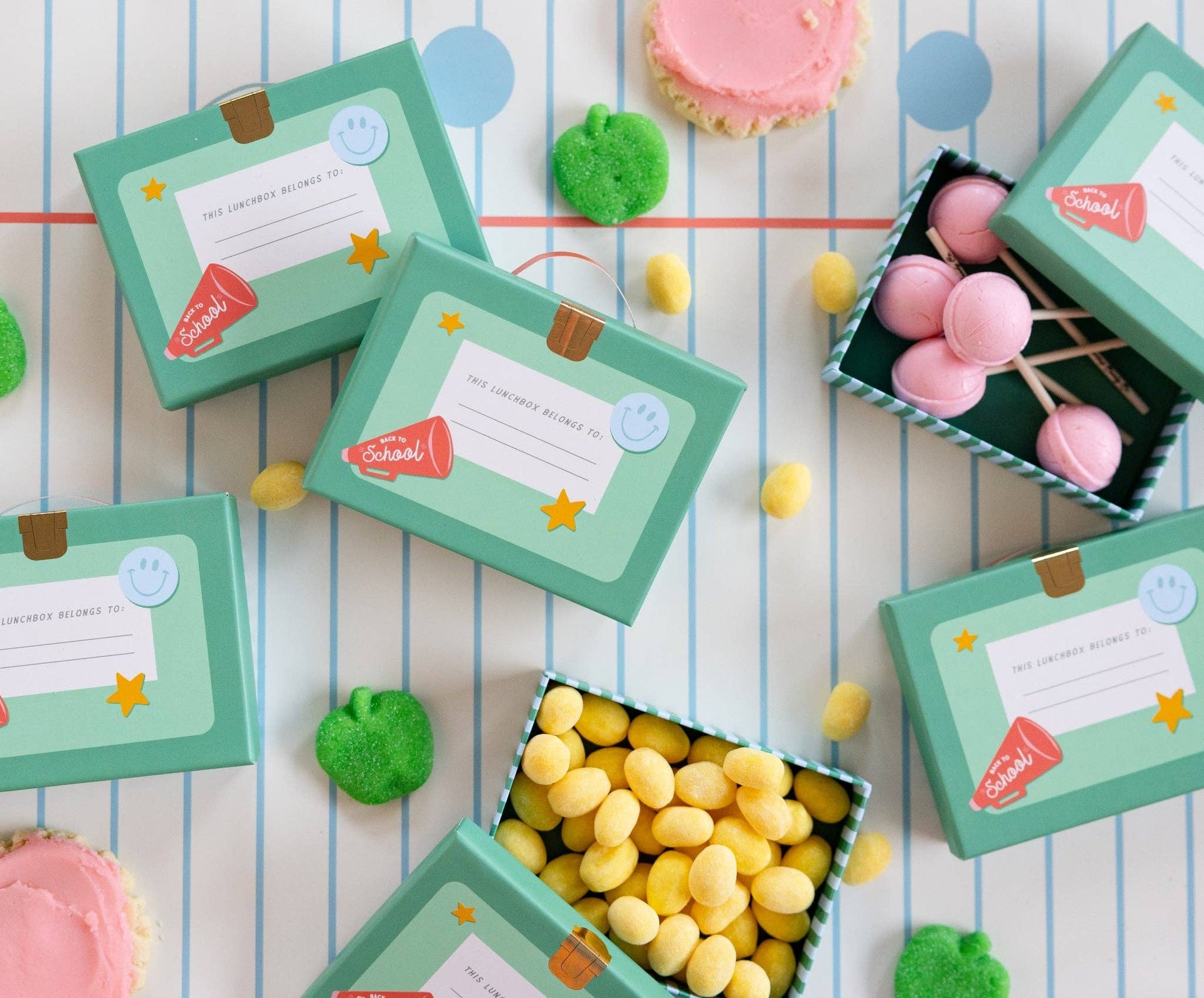Small green boxes with colorful candies and cookies on a striped background
