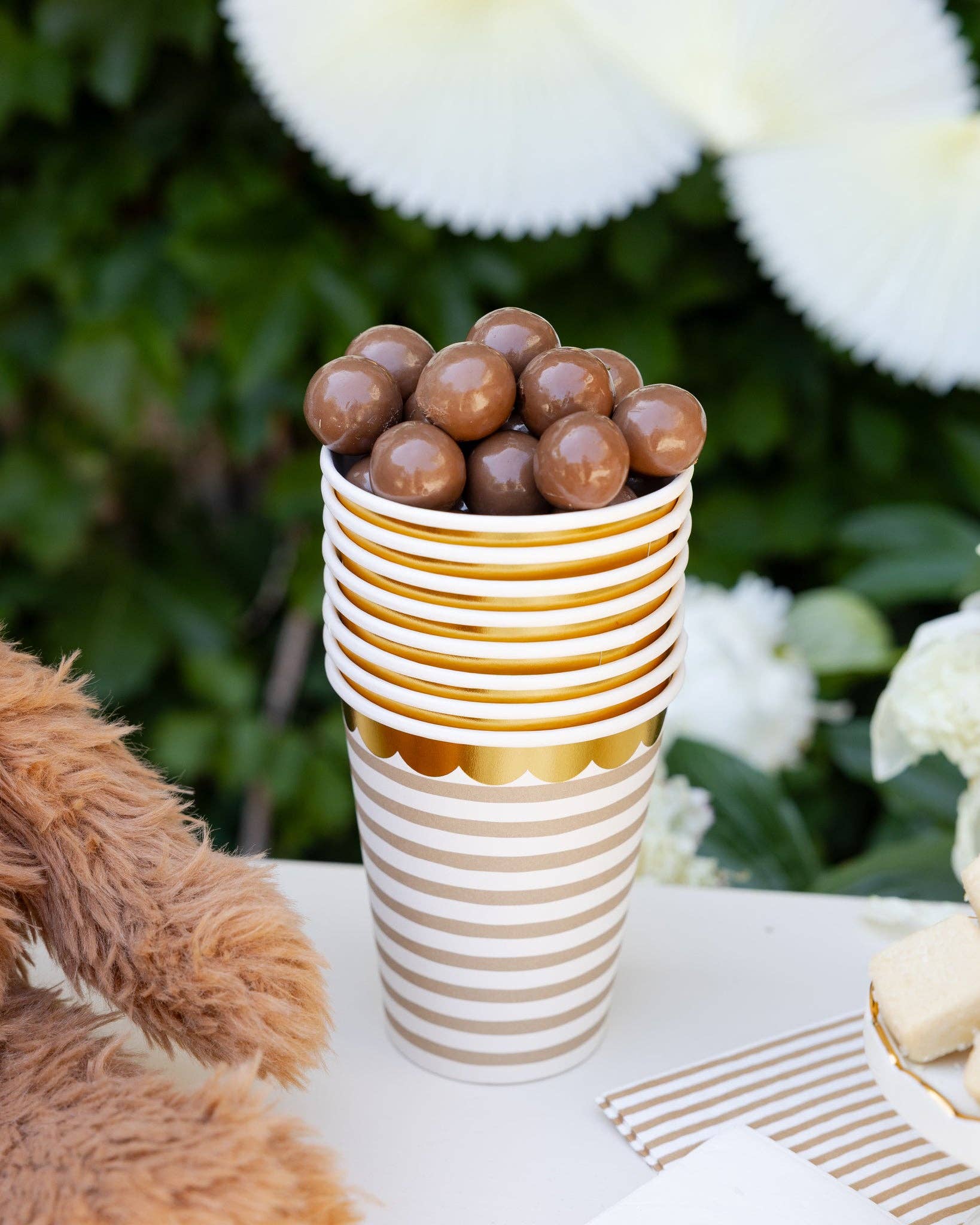 Striped paper cup filled with chocolate-covered candies on a table with flowers in the background