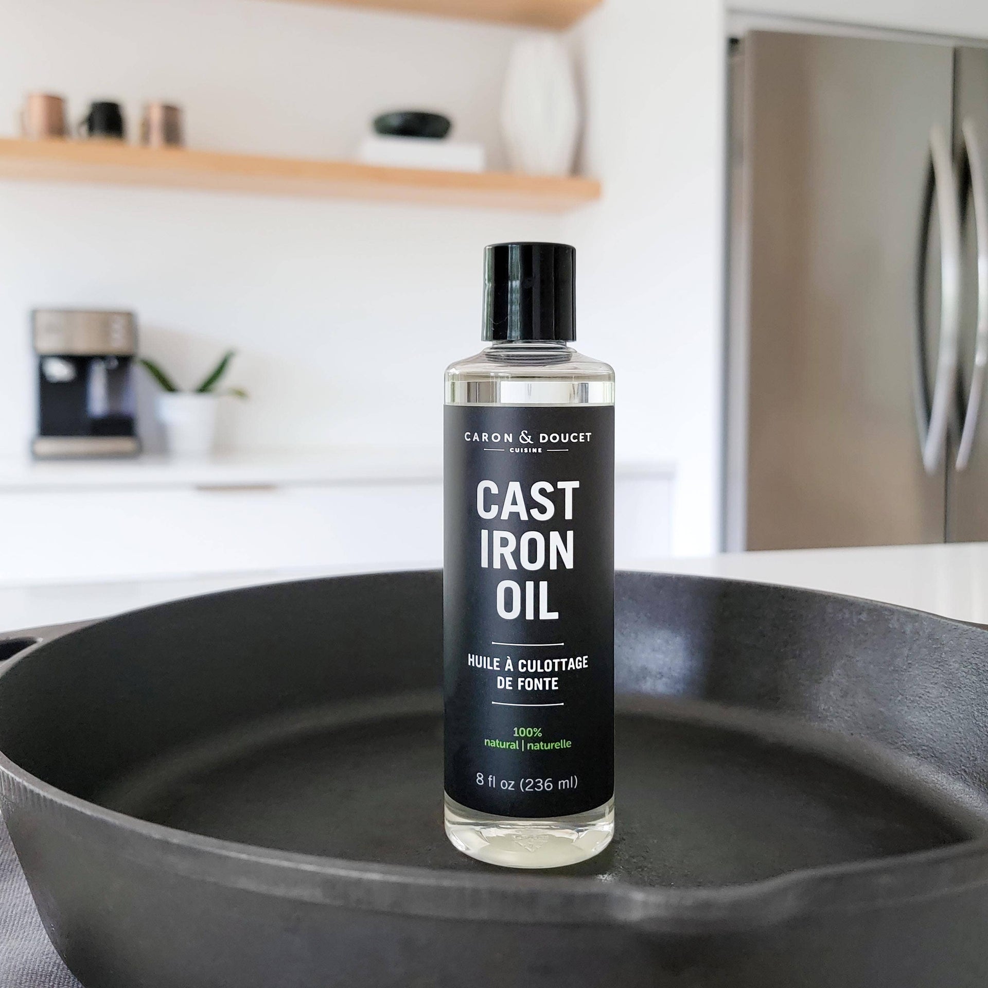 Bottle of Cast Iron Oil by Caron & Doucet on a cast iron skillet in a kitchen setting.