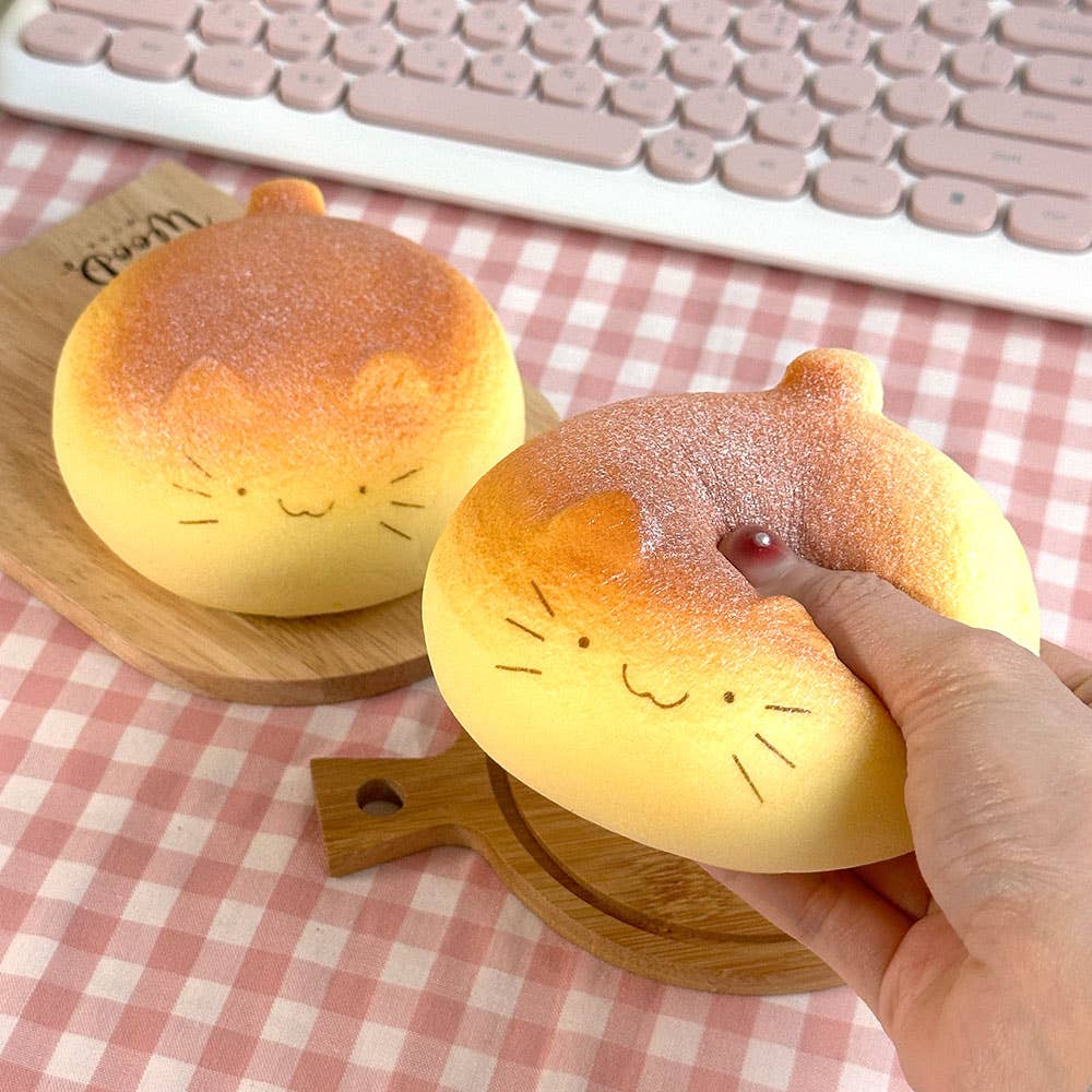 Two cat-shaped bread toys on a checkered tablecloth with a hand holding one.