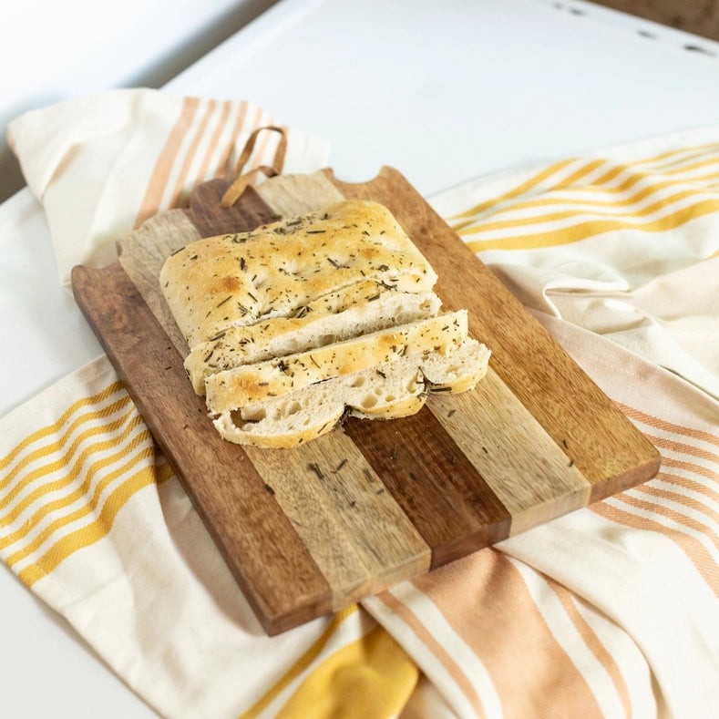 Loaf of bread sliced on a wooden serving board with a striped cloth underneath